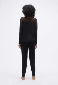 Σετ μαύρης άνετης ενδυμασίας με τοπ που τονίζεται με δαντέλα και έχει άνετη εφαρμογή, καθώς και παντελόνι με εφαρμοστά μανσέτες. Απαλό, υφασμένο υλικό.