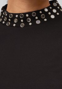 Czarny top z wysokim kołnierzem ozdobionym okrągłymi metalowymi ćwiekami oraz teksturowanymi okrągłymi akcentami w różnych rozmiarach. Miękka tkanina.