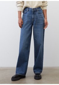 Niebieskie dżinsy z szerokimi nogawkami w średnim odcieniu, z wysokim stanem, zapięciem na guzik i kieszeniami z przodu, połączone z masywnymi czarnymi botkami na platformie.