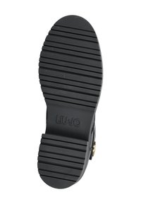 Suela de goma negra con surcos horizontales para tracción, con un tacón circular y el logotipo grabado "LIU JO" para la marca.