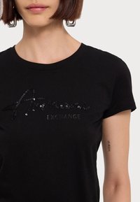 T-shirt in cotone nero con maniche corte, caratterizzato da un logo in paillettes tonali sulla parte anteriore e un collo a giro.