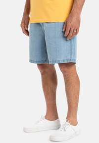 Lichtblauwe denim shorts met een ontspannen pasvorm, voorzien van een gestikte zoom en zakken. Draag ze met witte sneakers en een gele t-shirt.
