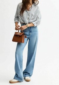 Striped, button-down shirt, loose fit; high-waisted, wide-leg blue jeans; brown handbag with gold hardware; white sneakers with tan soles.