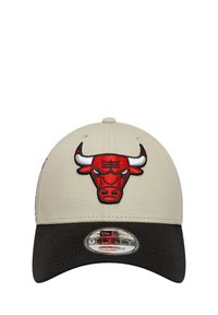 Gorra beige con visera negra, que presenta un logo de toro bordado en rojo. Incluye una pegatina de New Era en la parte delantera y correa trasera ajustable.
