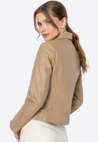 Beige Lederjacke mit passgenauer Form, Spitzenkragen und langen Ärmeln. Glatte Textur mit sichtbaren Nähten und taillierter Silhouette.