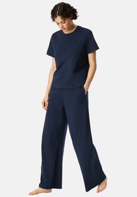 Marinblått lounge-set bestående av en t-shirt med kort ärm och vida byxor, tillverkat av mjukt material med en liten emblemdetalj.