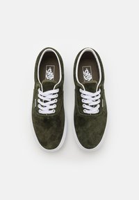 Zapatillas de ante verde con cordones blancos, con una punta redonda y superficie texturizada. Logotipo impreso en la plantilla marrón. Suela de goma blanca.