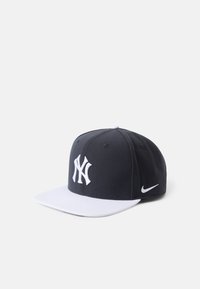 Ciemnoniebieska czapka z białym płaskim daszkiem, z haftowanym białym LOGO New York Yankees oraz akcentem w postaci logo Nike z boku.