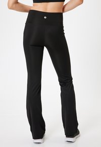 Leggings negras acampanadas de tela suave y elástica. Cintura alta con un pequeño logo en la parte posterior. Diseño elegante para uso atlético.