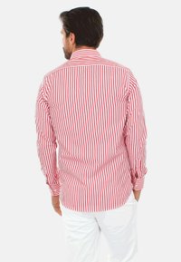 Camicia a righe rossa e bianca con maniche lunghe, caratterizzata da un colletto classico e orlo arrotondato, realizzata in tessuto leggero.