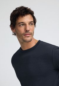 Camiseta negra de cuello redondo hecha de tejido de algodón suave. Presenta mangas cortas y un diseño simple y sin adornos.