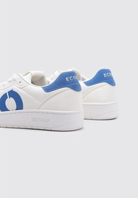 Zapatillas blancas con acentos azules, con un logo redondo en el lateral, suelas de goma texturizada y un acabado en piel lisa.