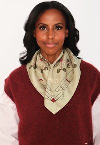 Silk skjerf i lys grønn med et geometrisk mønster, med røde detaljer og en tekstdetalj. Brukt sammen med en burgunder, fluffy genser.