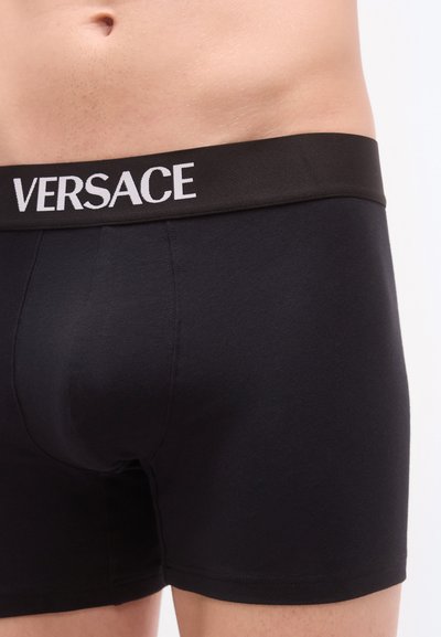 Boxer en coton noir à coupe ajustée. Comprend une large ceinture noire avec le logo "VERSACE" en blanc. Texture douce.