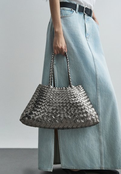 Πλεκτή μεταλλική ασημένια τσάντα χειρός με δύο πλεγμένες λαβές, τριγωνικό σχήμα και υφή. Συνδυάζεται με μια ελαφριά τζιν φούστα.