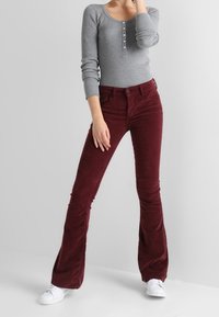 Kastanjefärgade kordflorsbyxor med vida ben, framfickor och knappstängning, ihop med en grå långärmad ribbad topp. Vita sneakers fulländar outfiten.