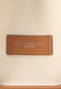 Borsa di tessuto beige con etichetta in pelle marrone con testo argentato impresso "GIANNI CHIARINI FIRENZE." Texture liscia, forma rettangolare.