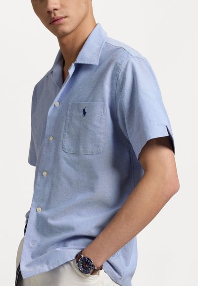 Ljusblå kortärmad skjorta med knäppning, gjord av strukturerad tyg, med en bröstficka och en liten mörk logotyp på vänster sida.