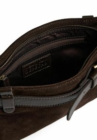 Mörkbrun mockaväska med läderrem, öppen toppdragkedja och innerväskficka med dragkedja som visar varumärkesetiketten "Couture Delépêche."