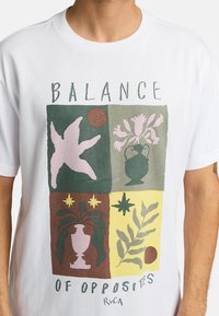 White cotton t-shirt featuring a graphic with four colored squares displaying plants and pottery in pink, green, brown, and yellow. Text reads "BALANCE OF OPPOSITES."