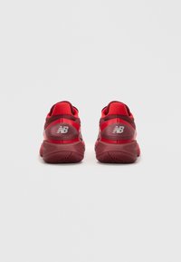 Et par røde New Balance løbesko set bagfra på en ensfarvet lys grå baggrund.