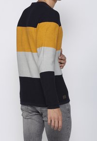 Tröja av pullovertyp med horisontella ränder i marinblått, gult, grått och vitt. Stickad textur, rund halsringning och en liten märkeslapp vid fållen.