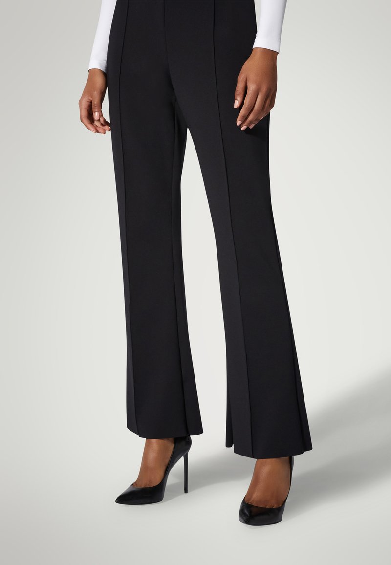 Svarta utsvängda byxor med en slät tygfinish, med vertikala sömmar och en subtil textur, i kombination med svarta spetsiga högklackade skor.