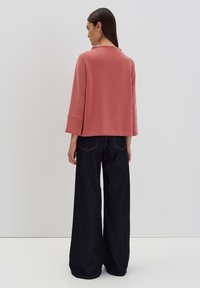 Light pink pullover sweater with a high neckline, three-quarter sleeves, and relaxed fit, paired with dark wide-leg jeans.