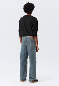 Μαύρο πουκάμισο με μακριά μανίκια και άνετο μπλε τζιν με ξεθωριασμένο πλύσιμο και πεντάτσεπη σχεδίαση, σε προβολή από πίσω.