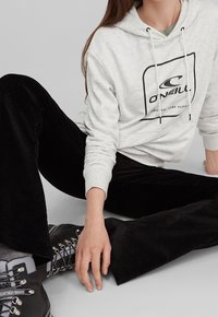 Donna seduta per terra con indosso una felpa O'Neill grigia chiara, pantaloni di corduroy neri, calzini grigi e stivali da escursionismo neri con lacci.