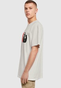 Lysegrå bomulds T-shirt med rund hals, korte ærmer, med sort og rød grafikdesign foran. Lige pasform.