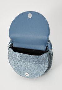 Geantă mică, rotundă, de umăr, cu clapetă deschisă din piele albastră și corp texturat din denim deschis, închidere cu capse din argint și capete de curea spiralate.
