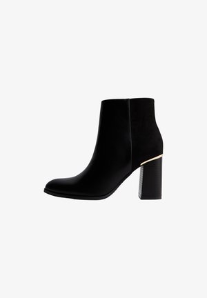 Bottines noires en cuir et daim avec un bout pointu et un talon épais, arborant un détail accent en or. Texture lisse sur l'ensemble.
