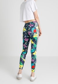 Blommiga leggings med en mörk bakgrund, prydda med gula, röda och lila blommor. Sidostraper i vitt. Matcher med en cropped vit skjorta.