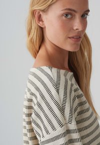 Black and white striped top with diagonal patterns, soft fabric, wide neckline, and short sleeves; features an overlapping shoulder design.