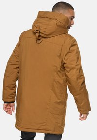 Parka aislante marrón con capucha, que presenta un alto cuello, un sistema de ajuste en el cuello y una tela texturizada y duradera.
