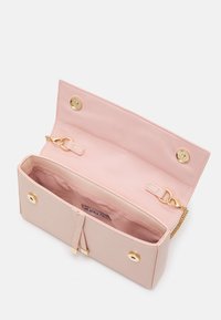 Light pink clutch purse open to show interior with gold magnetic snaps, chain strap, and brand label inside pocket.