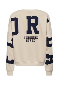 Sweat-shirt beige avec de grandes lettres noires "DR" au dos, la phrase "SUNSHINE STATE" en dessous, et des lettres noires supplémentaires sur les manches.