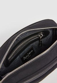 Černá látková kabelka se stříbrným zipem. Uvnitř se nachází malá kapsa na zip a nášivka s logem. Texturovaná podšívka se zopakovaným vzorem.