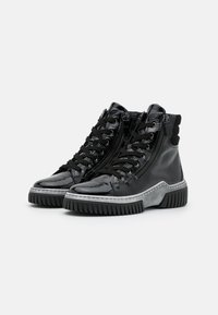 Zapatillas altas de charol negro con cremalleras laterales, cordones negros y suelas de goma gruesas en negro y gris.