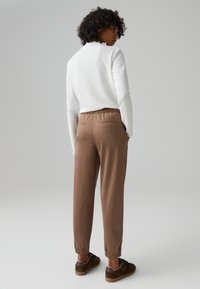 White textured pullover with frilled neck detail, paired with brown tapered joggers featuring an elastic waistband and side pockets.