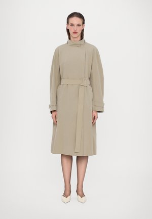 Manteau beige ceinturé avec un col montant et des manches surdimensionnées. Fabriqué dans un tissu lisse, il possède des poches latérales et arrive à mi-mollet.