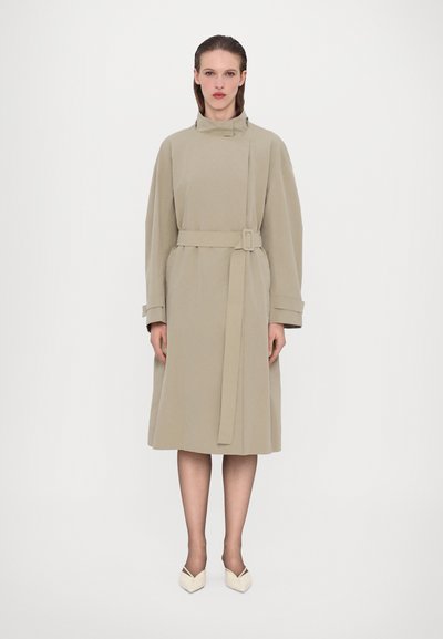 Beige geknoopte jas met een hoge kraag en oversized mouwen. Gemaakt van een gladde stof, heeft het zijzakken en komt het tot halverwege de kuit.