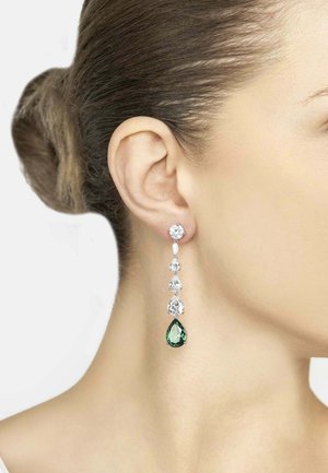 Woman’s ear with long drop earring featuring clear stones and a large pear-shaped green gemstone at the end.