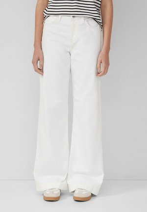 Jean large blanc taille haute, avec une fermeture à bouton et des passants de ceinture. Associé à un haut rayé et des baskets légères.
