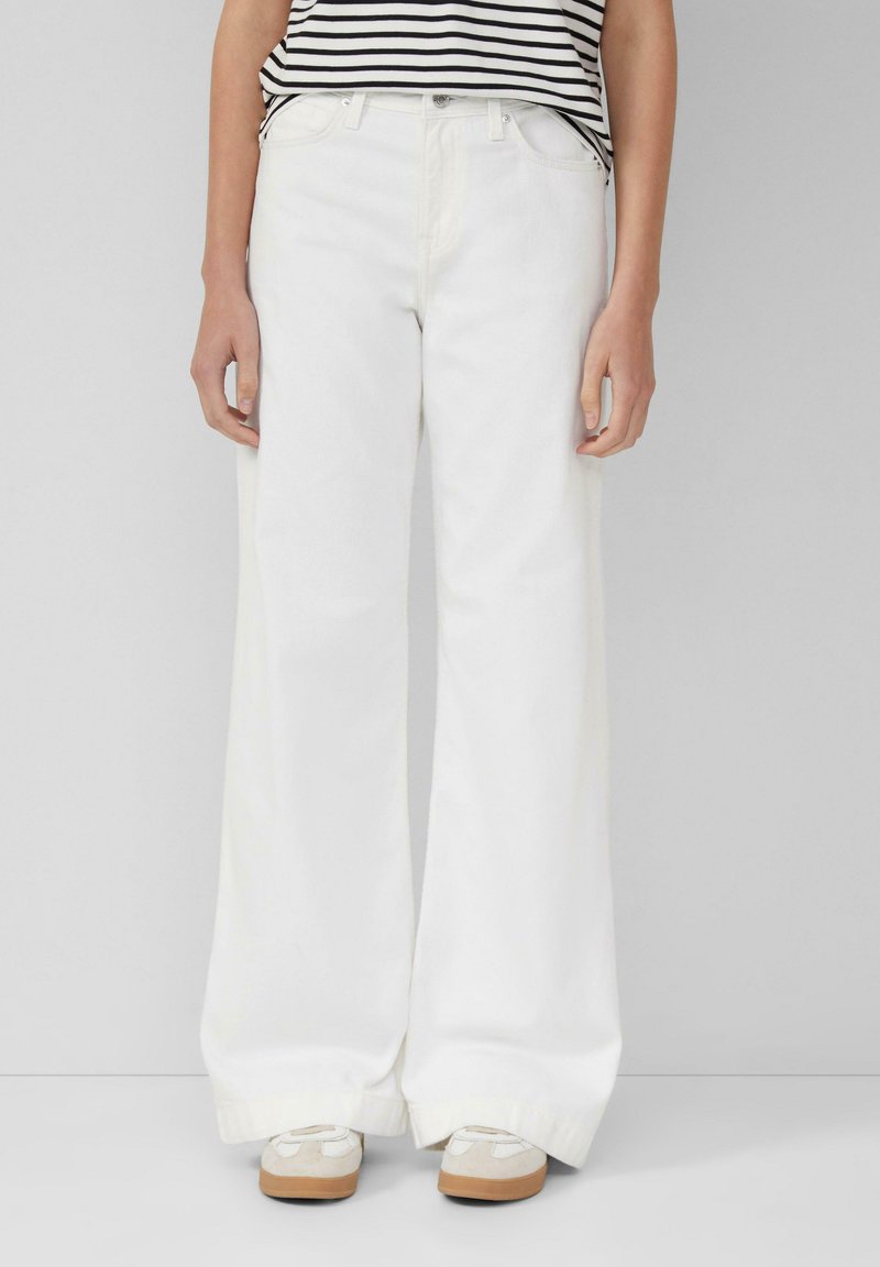 Witte wijde jeans met een hoge taille, voorzien van een knoopsluiting en riemlussen. Gecombineerd met een gestreept shirt en lichte sneakers.