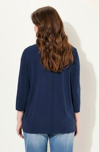 Haut à manches longues bleu marine à coupe décontractée, avec un détail de couture centrale et des poignets retournés, associé à un jean en denim bleu clair.