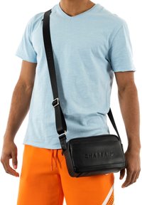 Borsa a tracolla nera con esterno in pelle liscia, logo impresso, cinturino regolabile e forma rettangolare, abbinata a pantaloni corti arancioni.