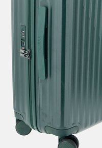 Valigia rigida verde con strisce verticali, maniglia laterale, lucchetto a combinazione e doppie ruote per una facile mobilità.