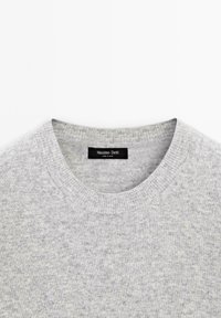 Szary dzianinowy sweter z okrągłym dekoltem, z teksturowanym wykończeniem i czarną metką marki wszytą wewnątrz kołnierza.